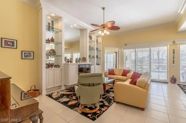 Living room with ceiling fan, light tile patterned floors, built in features, and ornamental molding
