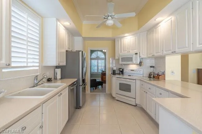 Kitchen featuring white appliances, white cabinets, sink, light tile patterned floors, and crown molding