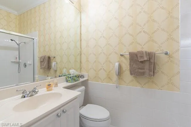 Bathroom featuring toilet, a shower with door, tile walls, crown molding, and vanity