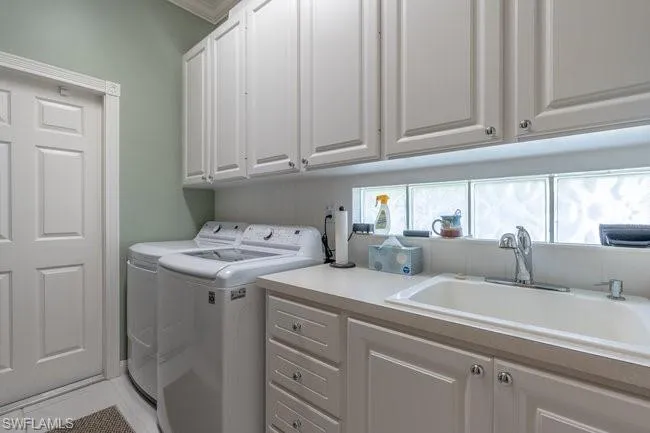 Laundry area with sink, tile patterned floors, independent washer and dryer, and cabinets