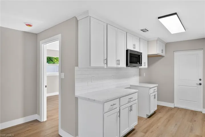 Kitchen with white cabinets, light wood finished floors, and stainless steel microwave