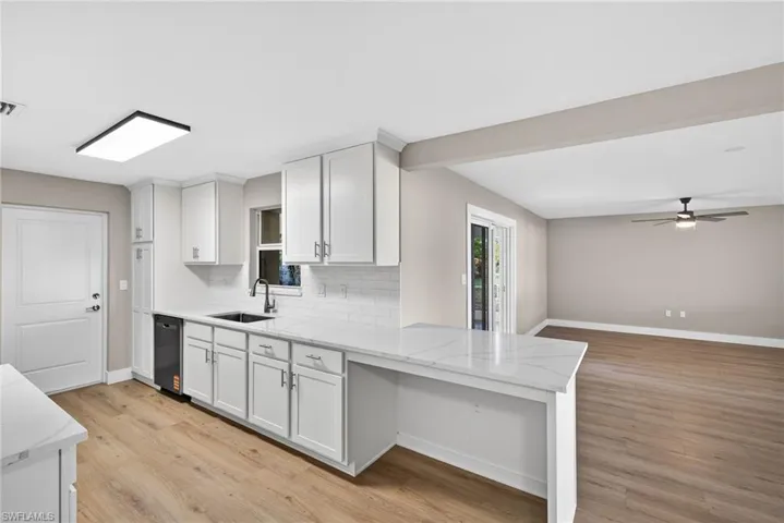 Kitchen featuring white cabinetry, light wood-style floors, decorative backsplash, light stone countertops, and a ceiling fan