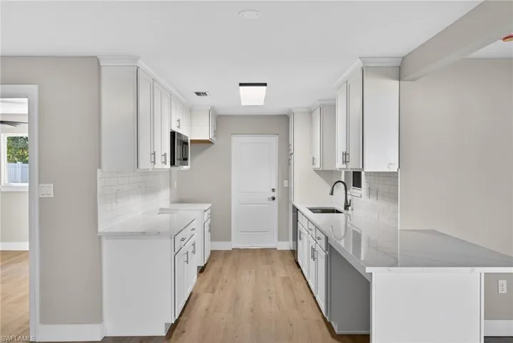 Kitchen with backsplash, light stone countertops, white cabinets, light wood-style floors, and appliances with stainless steel finishes