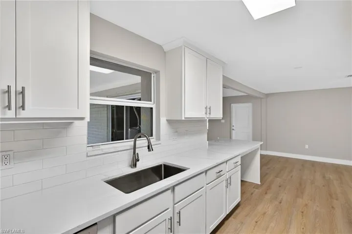Kitchen featuring white cabinetry, light wood finished floors, decorative backsplash, and light stone counters