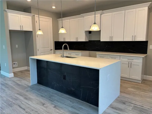 Kitchen with a kitchen island with sink, a sink, light wood-style floors, and tasteful backsplash