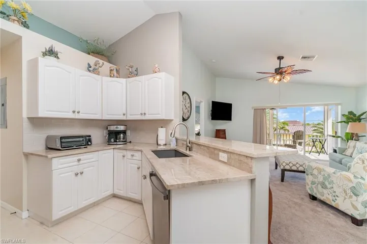 Kitchen with open floor plan, lofted ceiling, light stone countertops, backsplash, and a peninsula