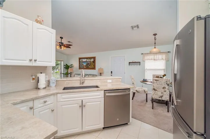 Kitchen featuring stainless steel appliances, white cabinets, light tile patterned floors, a peninsula, and light colored carpet