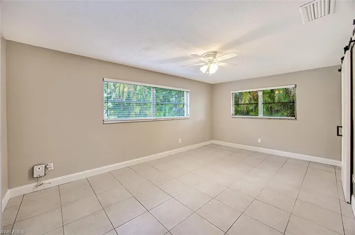 Empty room featuring a ceiling fan, visible vents, a barn door, and a healthy amount of sunlight