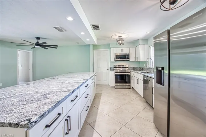 Kitchen featuring light stone counters, white cabinets, a sink, visible vents, and stainless steel appliances