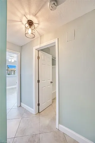 Hallway featuring baseboards, light tile patterned floors, and a textured ceiling