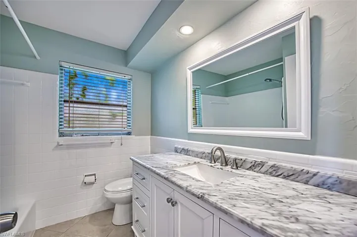 Bathroom with shower / bathtub combination, toilet, tile walls, tile patterned floors, and vanity