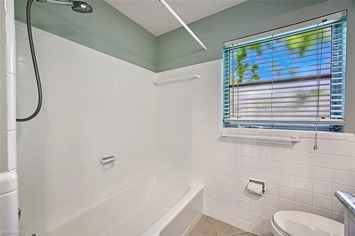Bathroom with toilet, tile patterned flooring, tile walls, and shower / bathing tub combination
