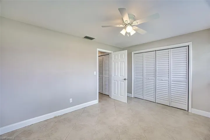 Unfurnished bedroom with light tile patterned floors, a closet, ceiling fan, visible vents, and baseboards