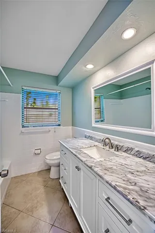Bathroom with tub / shower combination, toilet, tile walls, vanity, and tile patterned flooring