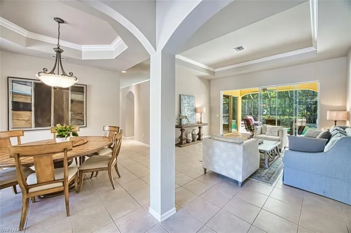 Living room featuring arched walkways, ornamental molding, light tile patterned floors, and a raised ceiling
