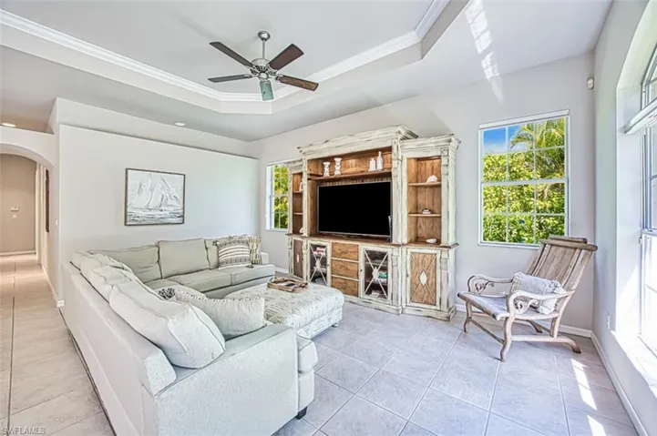 Living area featuring crown molding, ceiling fan, arched walkways, a tray ceiling, and light tile patterned floors