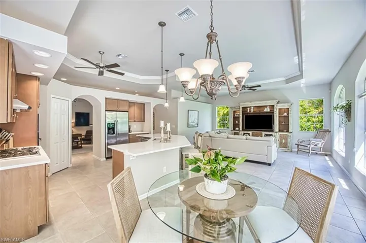 Dining area featuring a raised ceiling, arched walkways, ceiling fan with notable chandelier, and visible vents