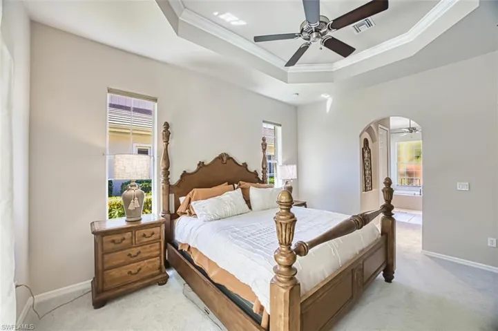Bedroom with a tray ceiling, multiple windows, arched walkways, and ornamental molding