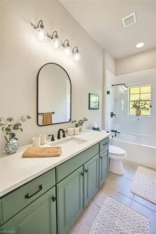 Bathroom with toilet, vanity, tile patterned flooring, tub / shower combination, and visible vents