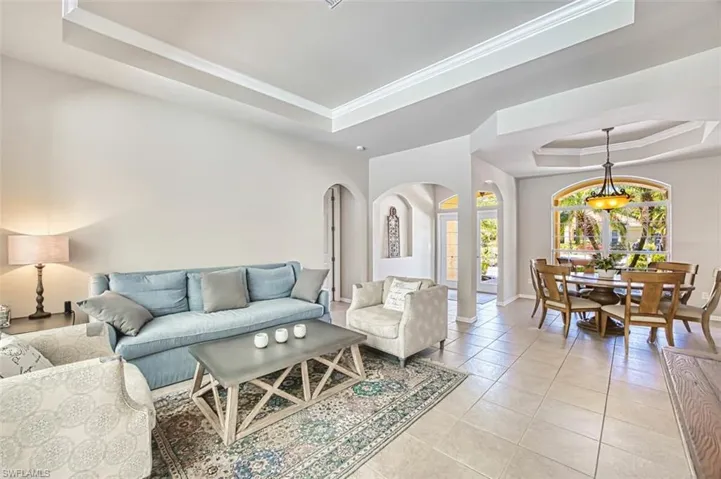 Living area featuring light tile patterned flooring, a raised ceiling, baseboards, arched walkways, and ornamental molding