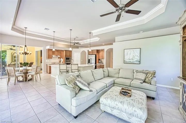 Living room featuring a tray ceiling, baseboards, ceiling fan with notable chandelier, arched walkways, and ornamental molding