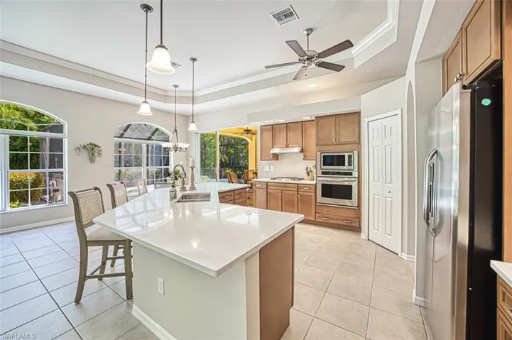 Kitchen featuring a tray ceiling, brown cabinetry, stainless steel appliances, visible vents, and ceiling fan