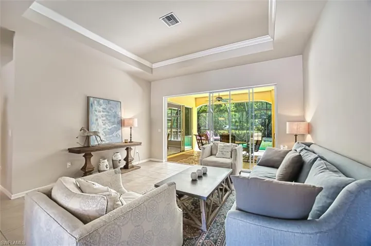 Living room featuring a raised ceiling, light tile patterned floors, crown molding, and visible vents