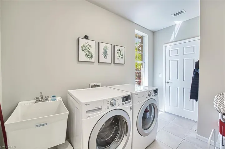 Laundry area featuring light tile patterned flooring, a sink, washing machine and clothes dryer, laundry area, and visible vents