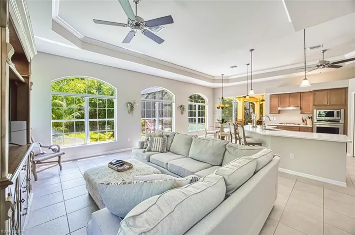 Living area featuring light tile patterned floors, baseboards, a raised ceiling, visible vents, and ceiling fan