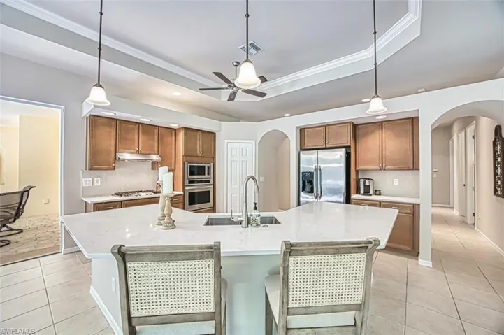 Kitchen featuring a tray ceiling, a sink, under cabinet range hood, stainless steel appliances, and arched walkways