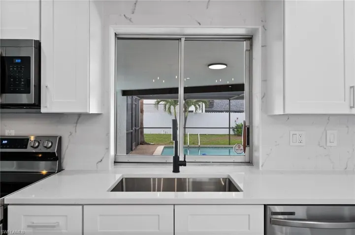 Kitchen with stainless steel appliances, a sink, white cabinetry, and light countertops