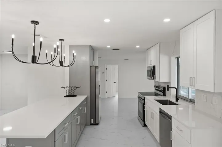 Kitchen featuring appliances with stainless steel finishes, a sink, a peninsula, recessed lighting, and light marble finish floors