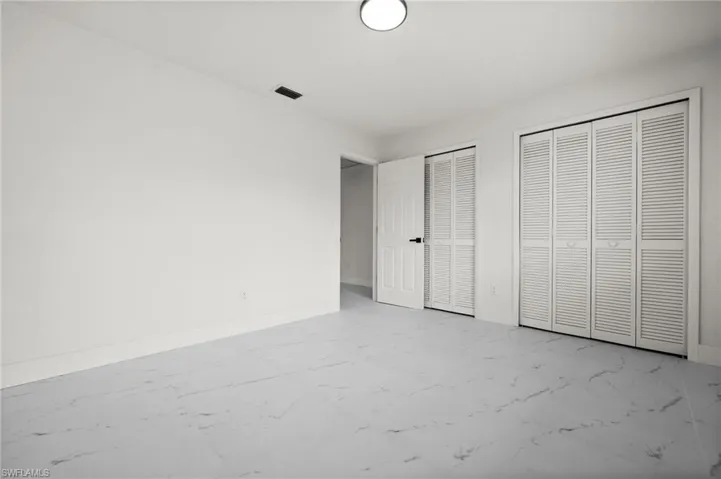 Unfurnished bedroom with multiple closets, light marble finish flooring, and baseboards