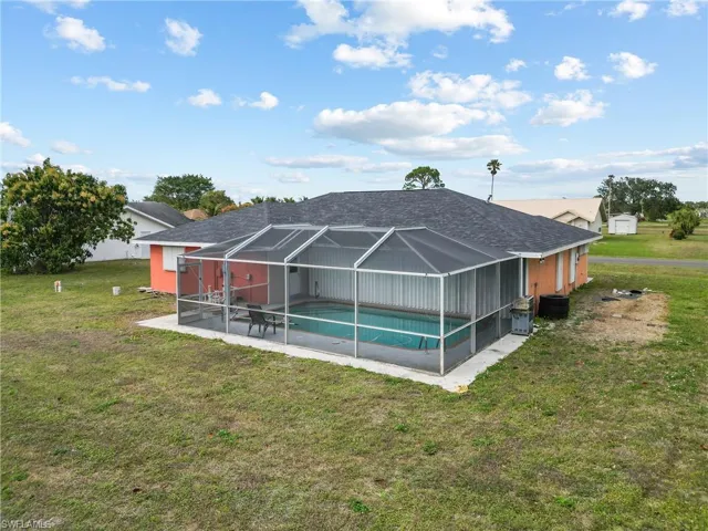 Rear view of property featuring a lawn, glass enclosure, and a patio area
