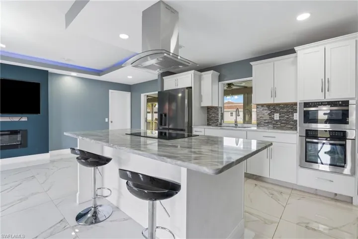 Kitchen with stainless steel appliances, island exhaust hood, sink, and white cabinets