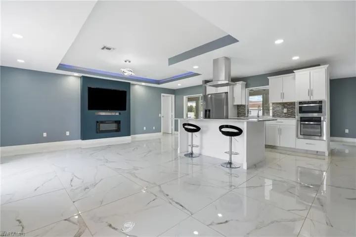 Kitchen featuring appliances with stainless steel finishes, a tray ceiling, a kitchen island, island exhaust hood, and white cabinets