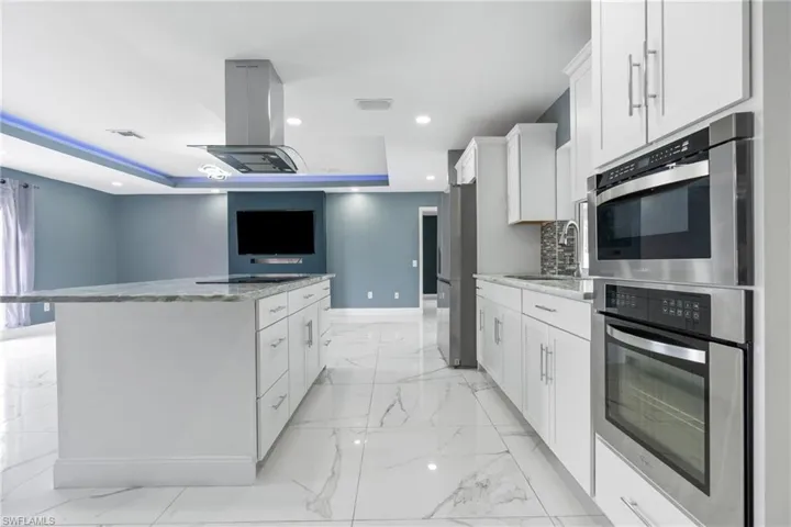 Kitchen featuring stainless steel fridge, island exhaust hood, light stone counters, white cabinets, and a kitchen island