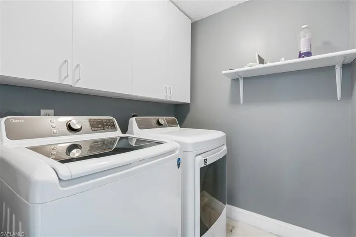 Clothes washing area with separate washer and dryer, cabinets, and a textured ceiling