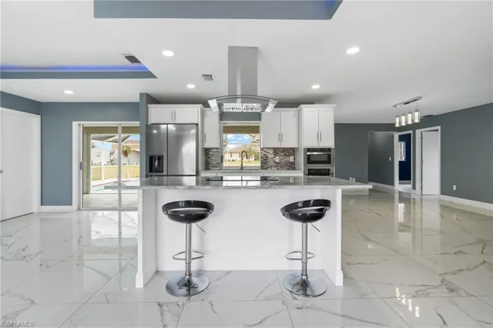 Kitchen with white cabinetry, backsplash, stainless steel fridge, and island exhaust hood