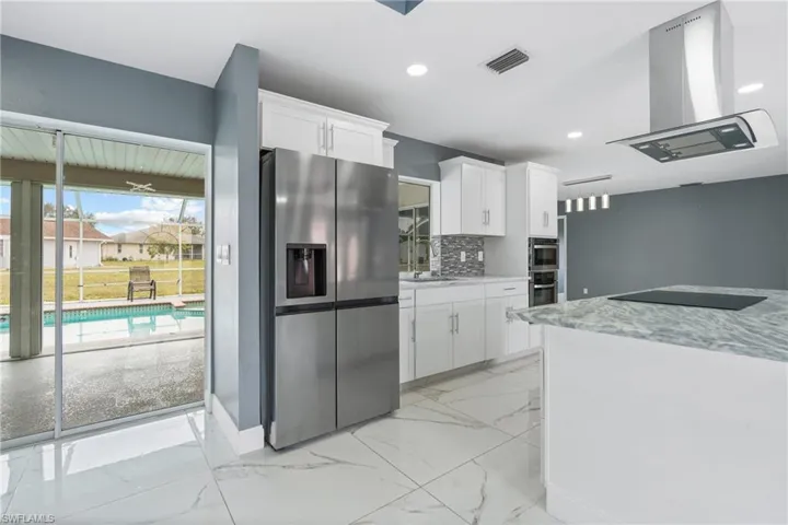 Kitchen with white cabinets, island exhaust hood, tasteful backsplash, and stainless steel fridge