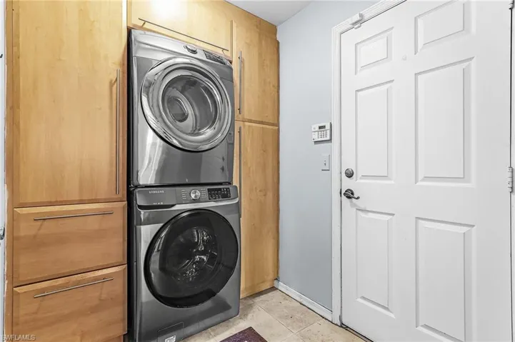 Laundry room with cabinet space, stacked washing machine and dryer, and light tile patterned floors