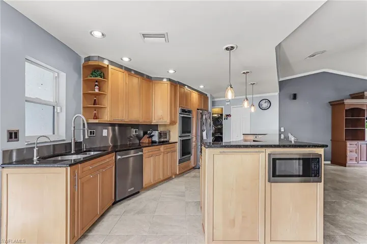 Kitchen featuring open shelves, dark stone counters, a kitchen island, stainless steel appliances, and crown molding