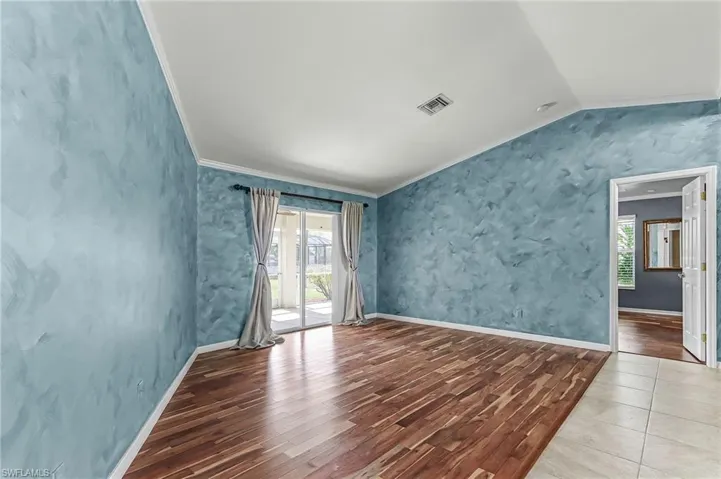 Empty room with crown molding, wood finished floors, and vaulted ceiling