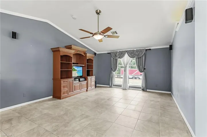 Unfurnished living room with ceiling fan, ornamental molding, vaulted ceiling, and light tile patterned floors