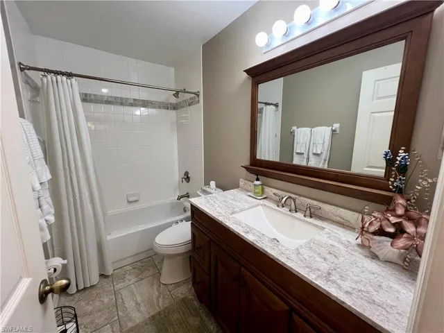 Full bathroom with vanity, shower / bathtub combination with curtain, toilet, and tile patterned flooring