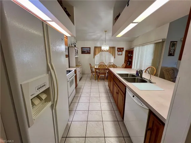 Kitchen featuring white appliances, an inviting chandelier, light tile patterned flooring, hanging light fixtures, and sink