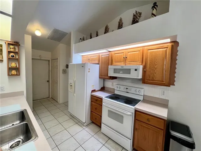 Kitchen with lofted ceiling, white appliances, light tile patterned floors, sink, and backsplash