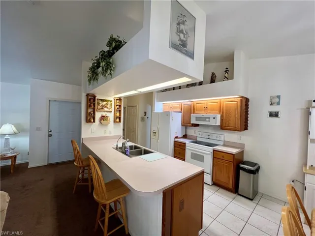 Kitchen with kitchen peninsula, light tile patterned flooring, white appliances, sink, and a breakfast bar area