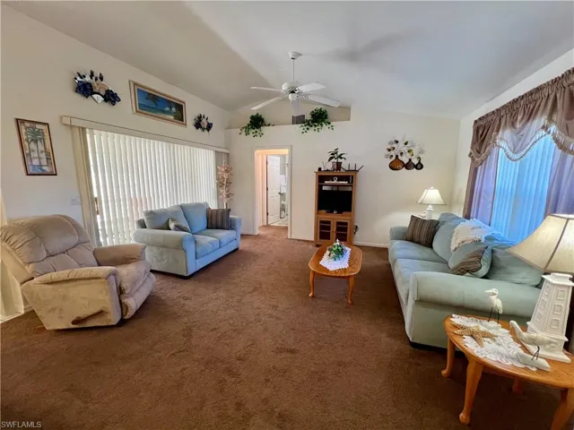Living room featuring ceiling fan, carpet flooring, and vaulted ceiling