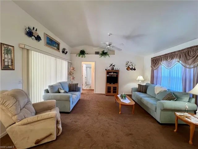 Carpeted living room featuring ceiling fan, a wealth of natural light, and lofted ceiling
